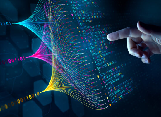 A human hand points towards a vibrant digital data visualization featuring colorful wave-like patterns and binary code. The setting is futuristic and tech-oriented, with a dark background emphasizing the glowing visuals. The image conveys innovation, technology, and data analysis concepts.